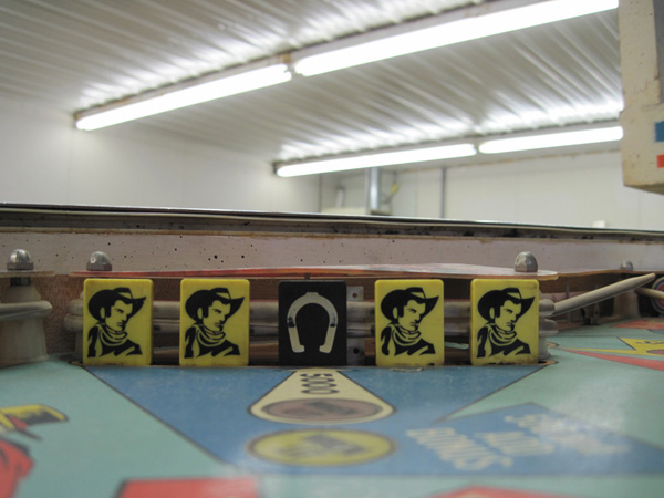 The left side drop targets. Four are yellow, with an image of a cowboy on them. The middle target is black, with the image of a horseshoe on it.