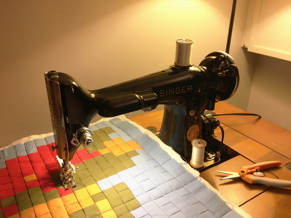 A front view of the Singer 201. A small quilt depicting a low-resolution "pixelated" Mario figure is under the presser foot.